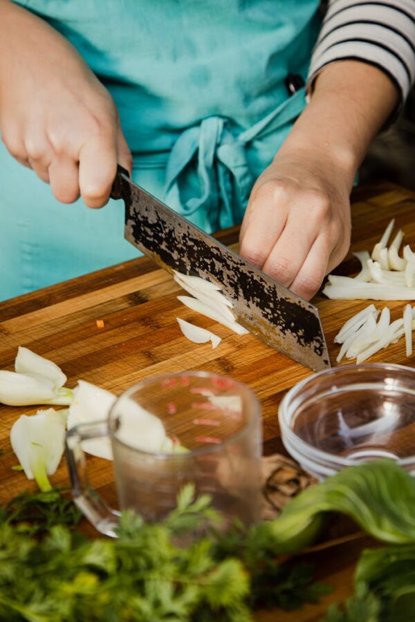 Close-up of chef's hands chopping onions on a wooden cutting board in a kitchen setting.